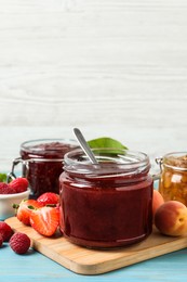 Photo of Jars with different jams and fresh fruits on light blue wooden table