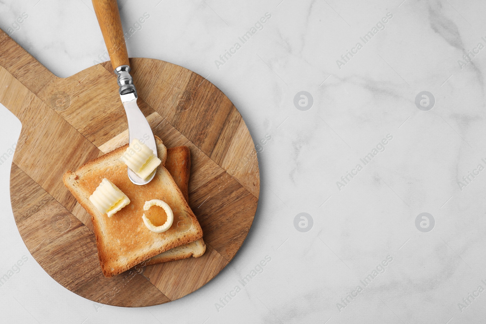 Photo of Tasty butter curls, knife and toasts on white marble table, top view. Space for text