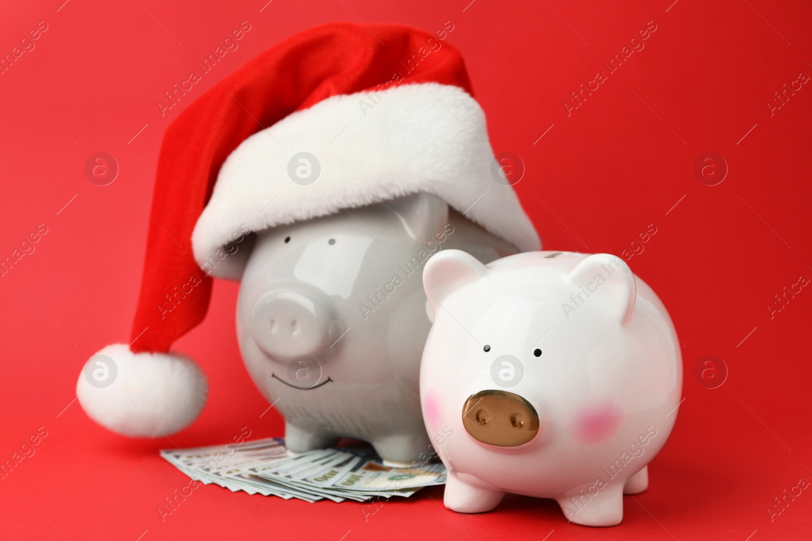 Photo of Piggy banks with Santa hat and dollar banknotes on red background