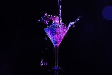 Photo of Pouring martini. Glass and splashes in neon lights on dark background, bokeh effect