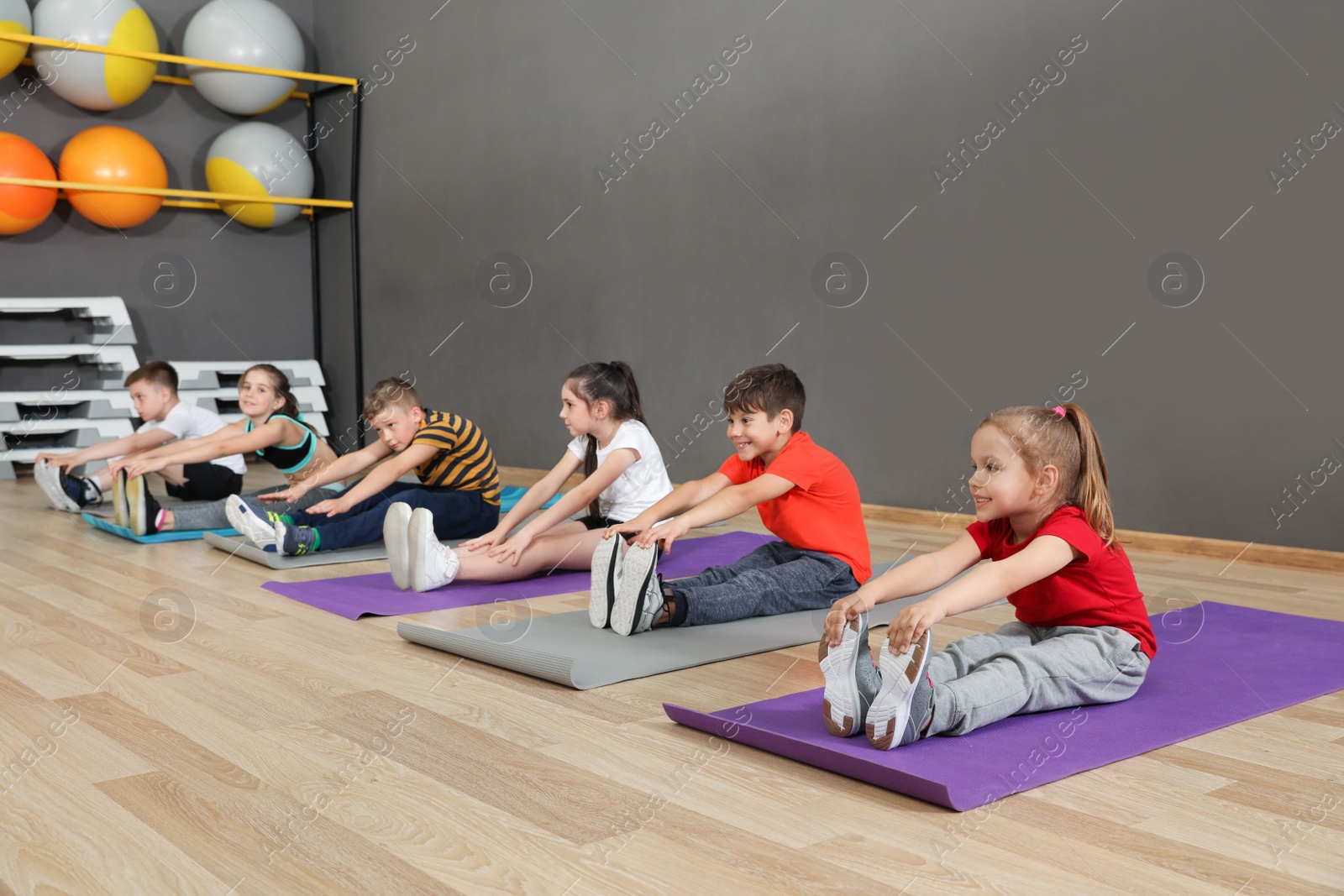 Photo of Cute little children sitting on floor and doing physical exercise in school gym. Healthy lifestyle