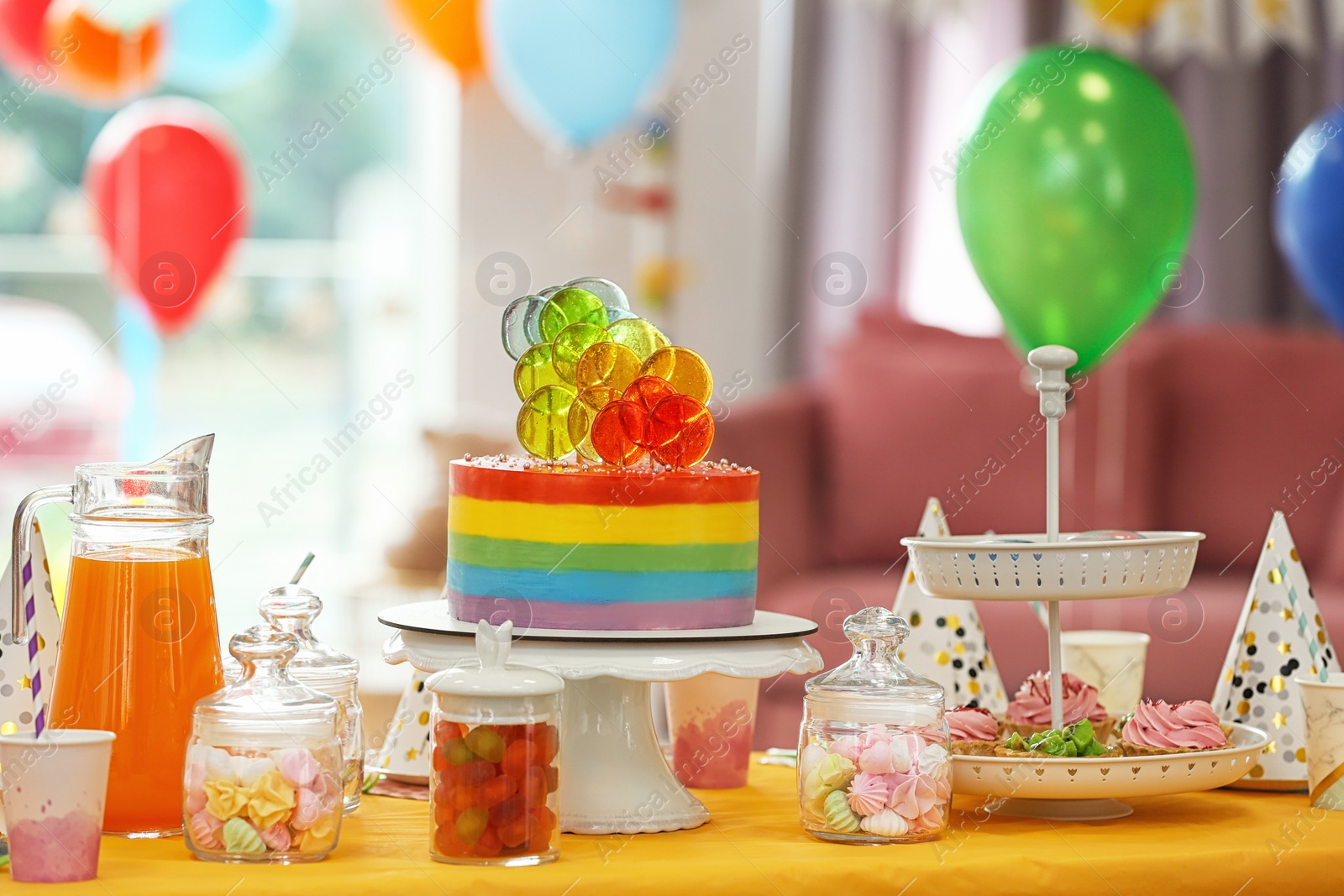 Photo of Bright birthday cake and other treats on table in decorated room