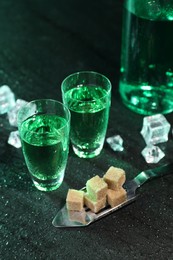 Photo of Absinthe in shot glasses, spoon, brown sugar and ice cubes on gray table. Alcoholic drink