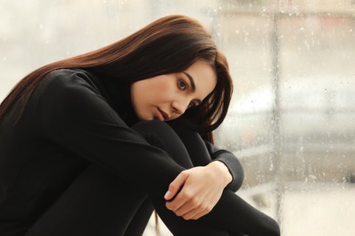 Photo of Depressed woman near window on rainy day