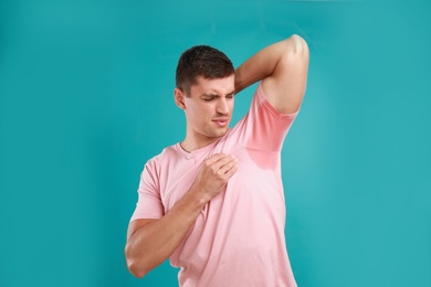 Photo of Young man with sweat stain on his clothes against light blue background. Using deodorant