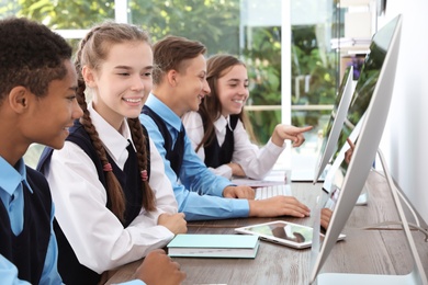 Photo of Teenage students in stylish school uniform at desks with computers