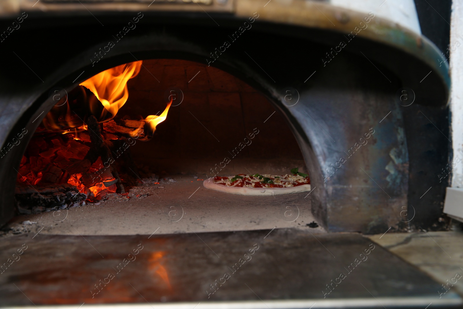 Photo of Burning firewood and tasty pizza in oven at restaurant kitchen