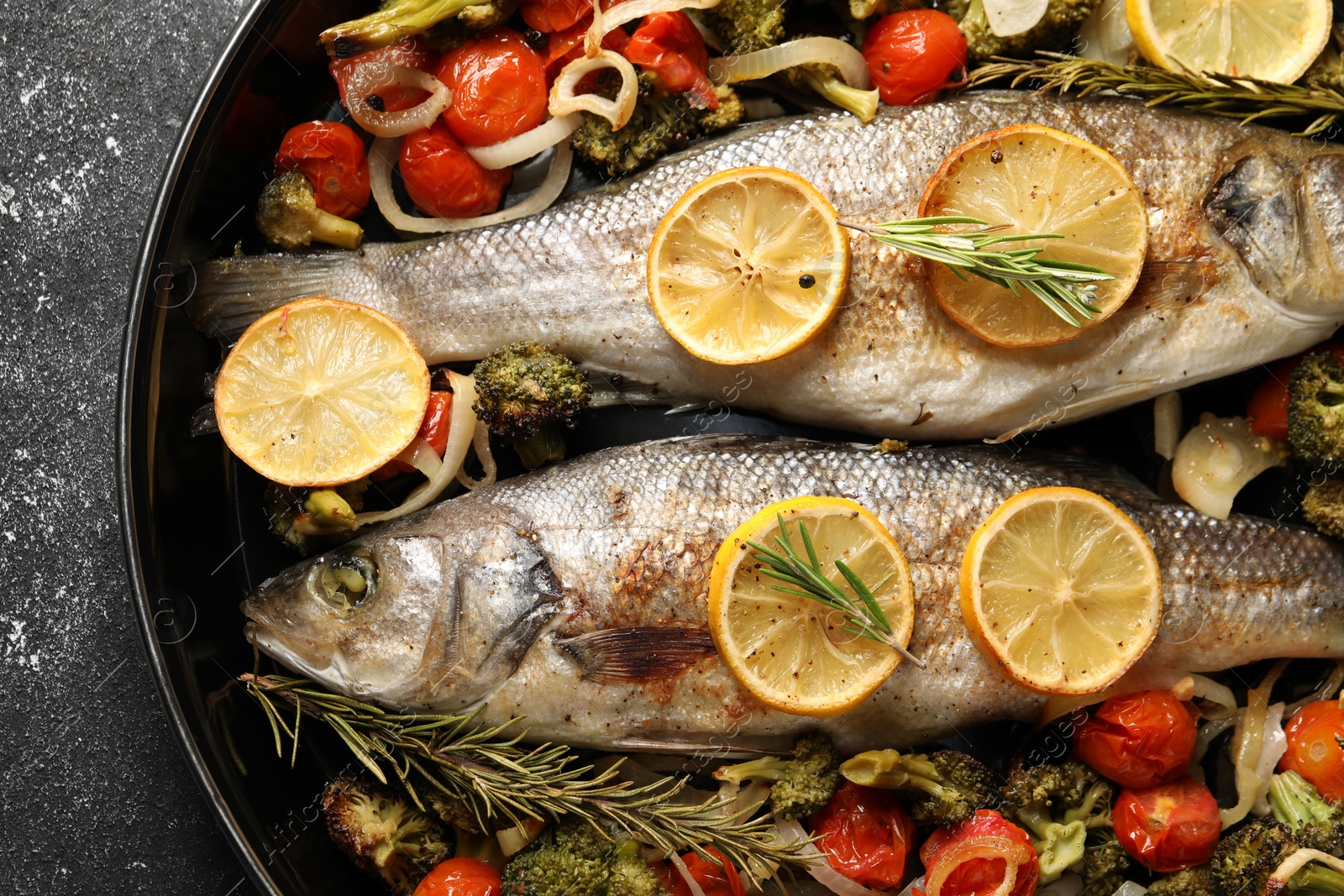 Photo of Baked fish with vegetables, rosemary and lemon on black textured table, top view