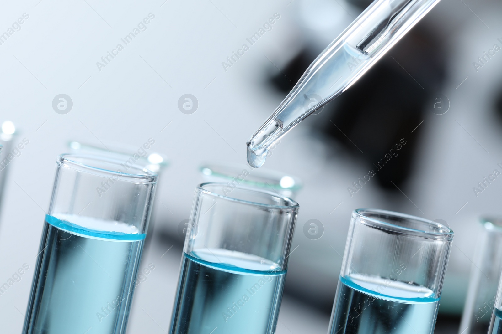 Photo of Dripping liquid from pipette into test tube on blurred background, closeup