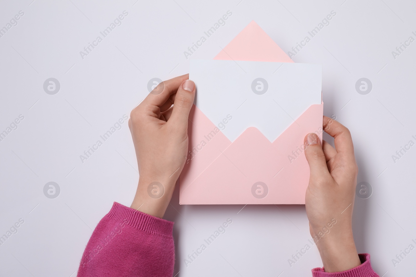 Photo of Woman holding letter envelope with card at white table, top view