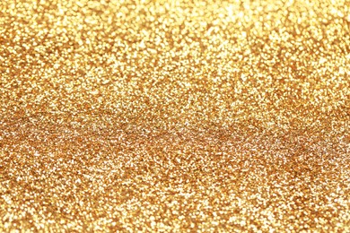 Photo of Beautiful golden shiny glitter as background, closeup