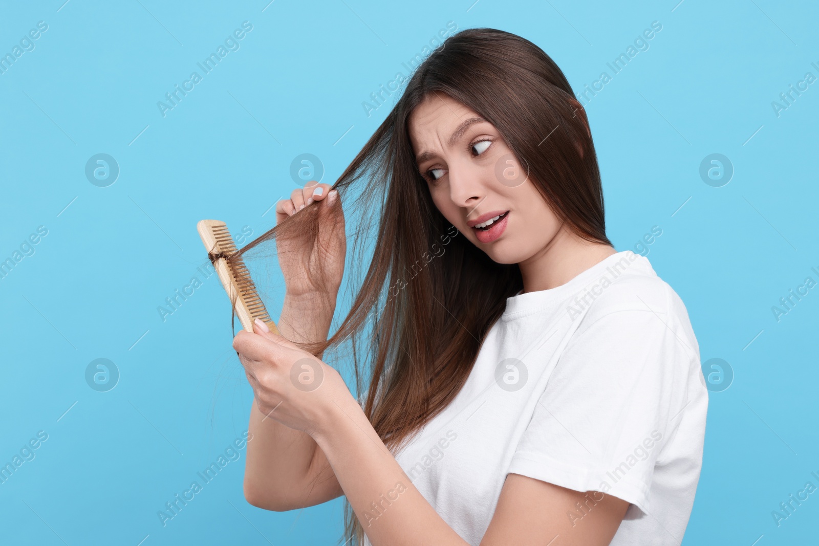 Photo of Upset woman brushing her hair on light blue background. Alopecia problem