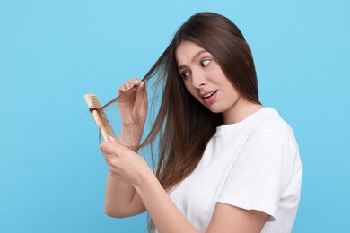 Upset woman brushing her hair on light blue background. Alopecia problem