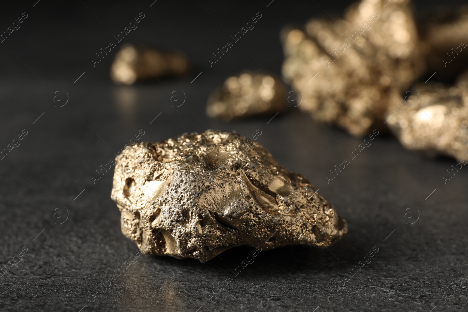 Photo of Shiny gold nugget on grey textured surface, closeup