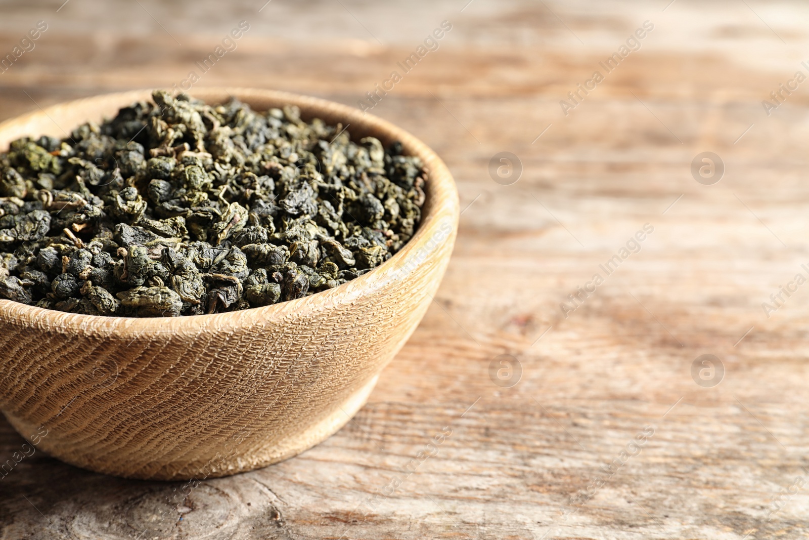 Photo of Bowl of Tie Guan Yin oolong tea leaves on wooden background, closeup. Space for text