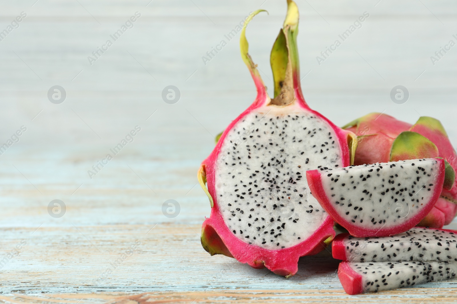 Photo of Delicious cut and whole dragon fruits (pitahaya) on light wooden table. Space for text