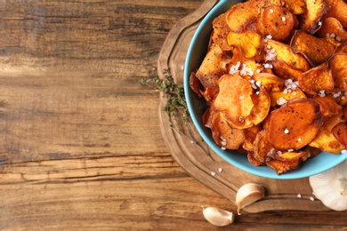 Photo of Bowl of sweet potato chips on wooden table, top view. Space for text