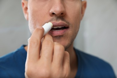 Photo of Man applying hygienic lip balm on grey background, closeup