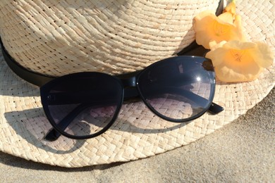 Photo of Hat with beautiful sunglasses and flowers on sand, closeup