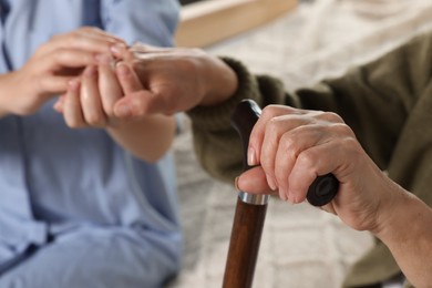 Photo of Caregiver and elderly woman with walking cane at home, closeup