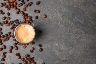 Photo of Cup of tasty espresso and scattered coffee beans on grey table, flat lay. Space for text