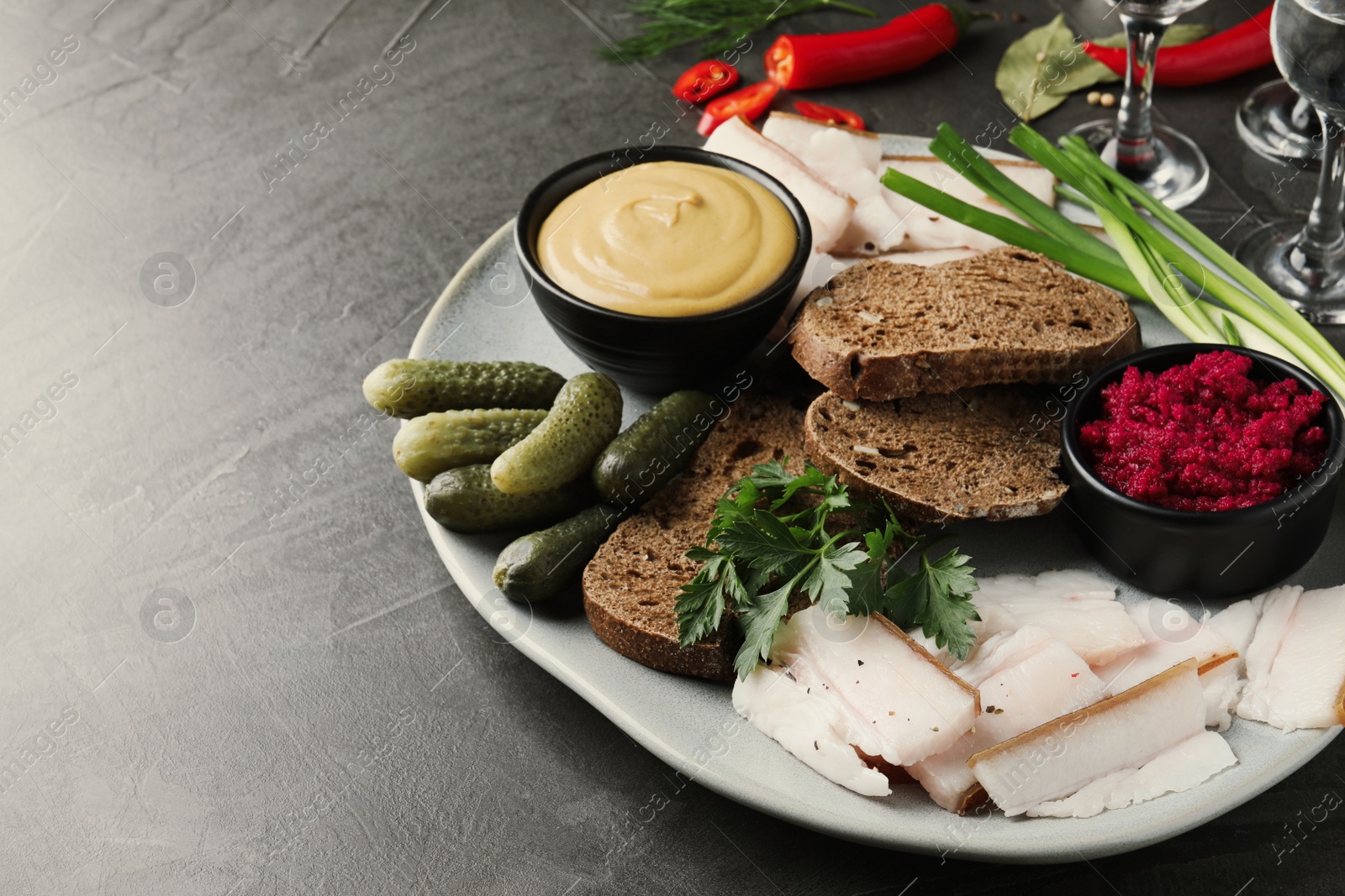 Photo of Tasty salt pork with rye bread and sauces served on grey table, space for text