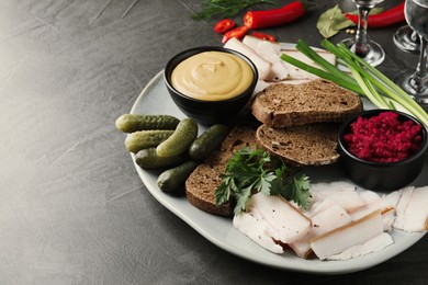 Photo of Tasty salt pork with rye bread and sauces served on grey table, space for text