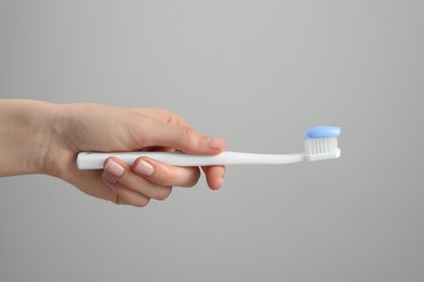 Woman holding toothbrush with paste on light grey background, closeup