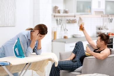 Lazy husband watching TV and his tired wife ironing at home