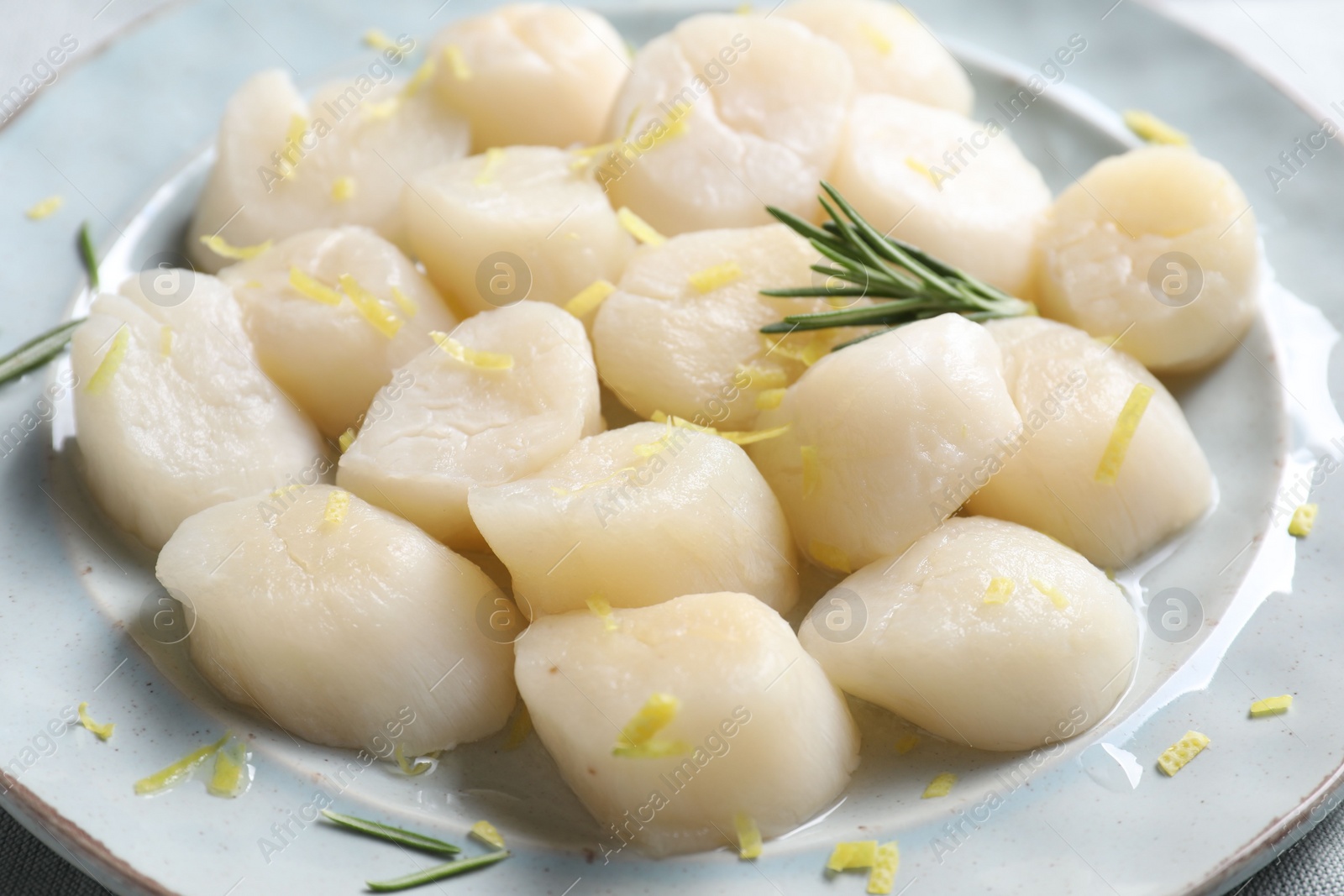 Photo of Raw scallops with lemon zest and rosemary on plate, closeup