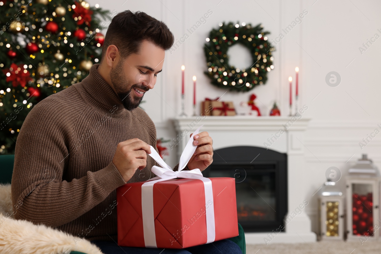 Photo of Happy young man opening Christmas gift at home