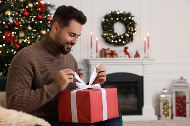 Happy young man opening Christmas gift at home