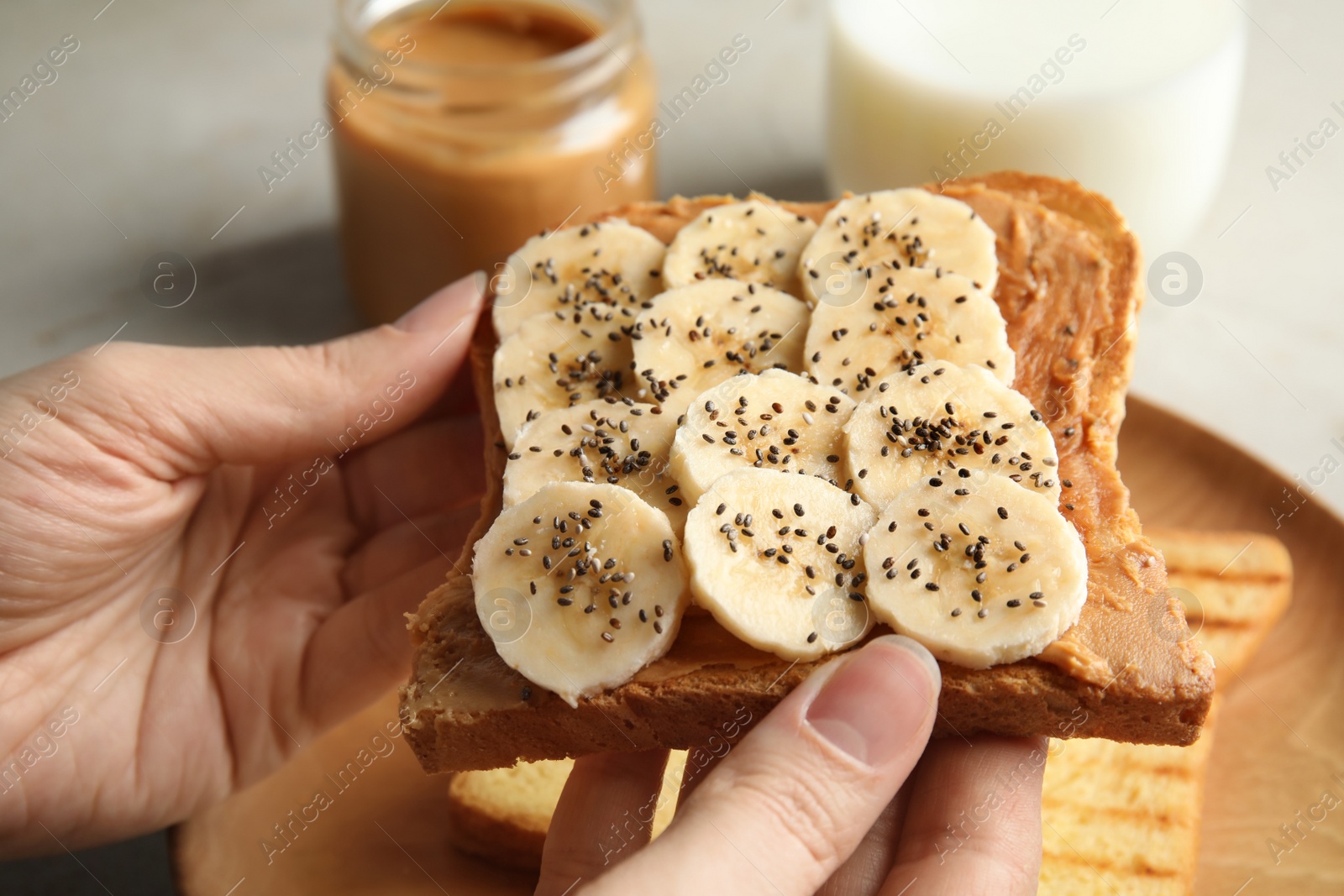 Photo of Woman eating toast with banana, peanut butter and chia seeds at table, closeup