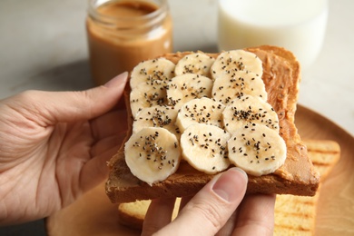 Woman eating toast with banana, peanut butter and chia seeds at table, closeup