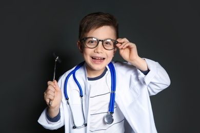 Photo of Cute little child in doctor uniform with reflex hammer on black background