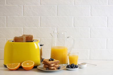 Modern toaster and tasty breakfast on white table near brick wall