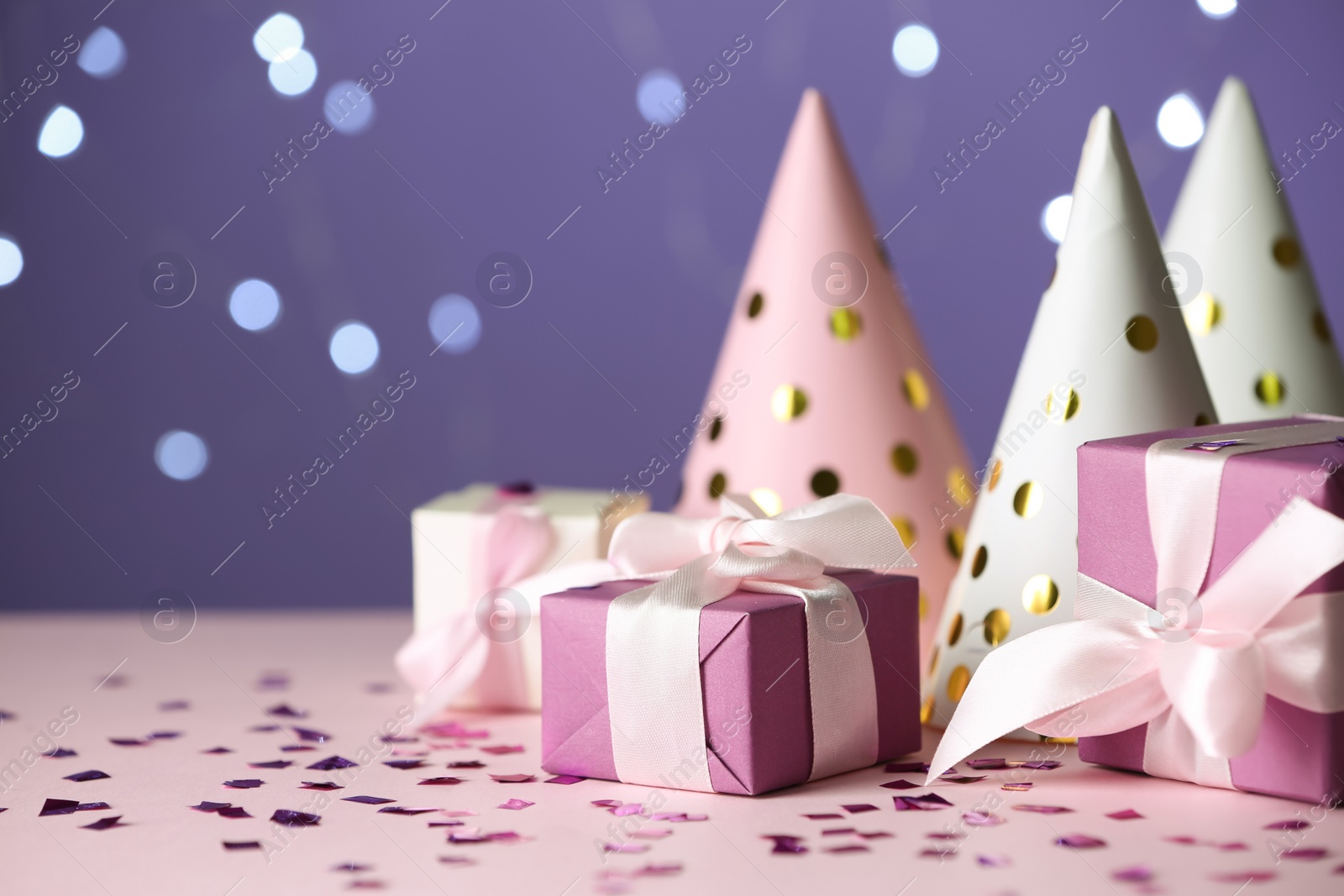 Photo of Gift boxes and party hats on pink table against blurred lights. Space for text