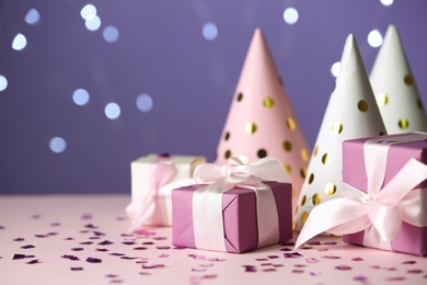 Gift boxes and party hats on pink table against blurred lights. Space for text