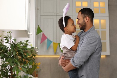 Photo of Happy African American father and his cute son in bunny ears headband in kitchen. Easter celebration