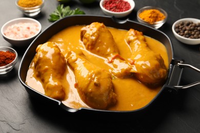 Photo of Tasty chicken curry and ingredients on black textured table, closeup