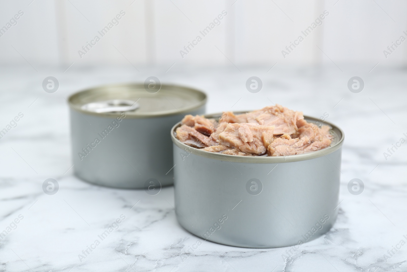 Photo of Tin cans with canned tuna on white marble table, closeup
