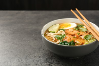 Photo of Delicious ramen with shrimps and chopsticks on grey table, closeup with space for text. Noodle soup