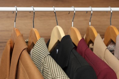 Photo of Hangers with stylish women`s clothes on rack near wooden wall, closeup