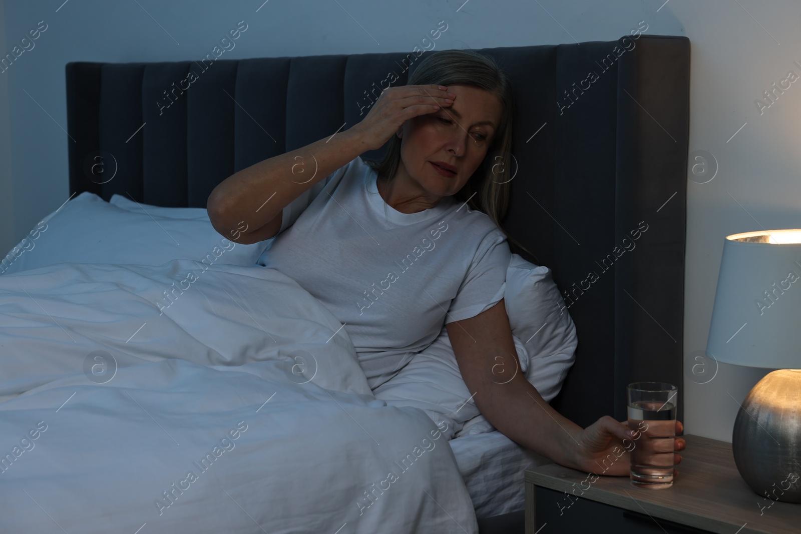 Photo of Woman with glass of water suffering from headache in bed at night