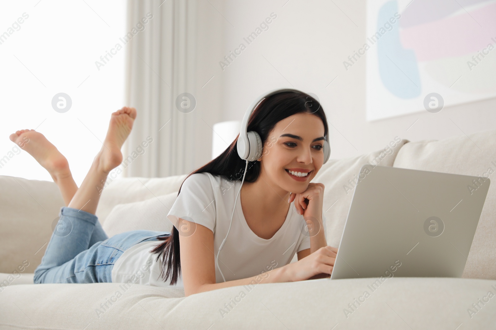 Photo of Woman with laptop and headphones lying on sofa at home