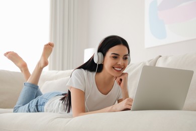 Photo of Woman with laptop and headphones lying on sofa at home