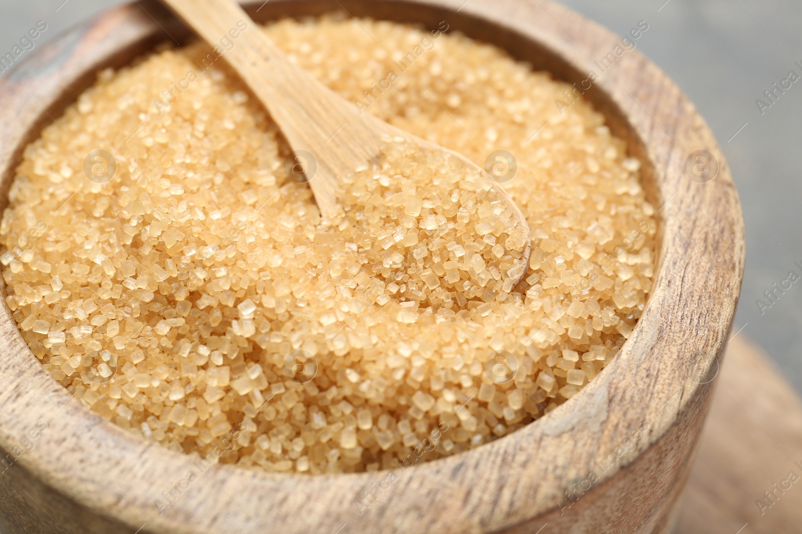 Photo of Brown sugar in bowl and spoon on blurred background, closeup