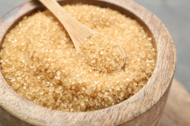 Brown sugar in bowl and spoon on blurred background, closeup