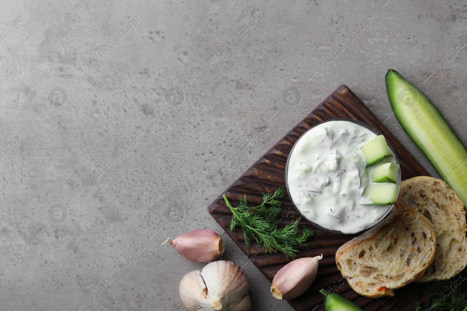 Photo of Tzatziki cucumber sauce with garlic, dill and bread on grey background, top view. Space for text