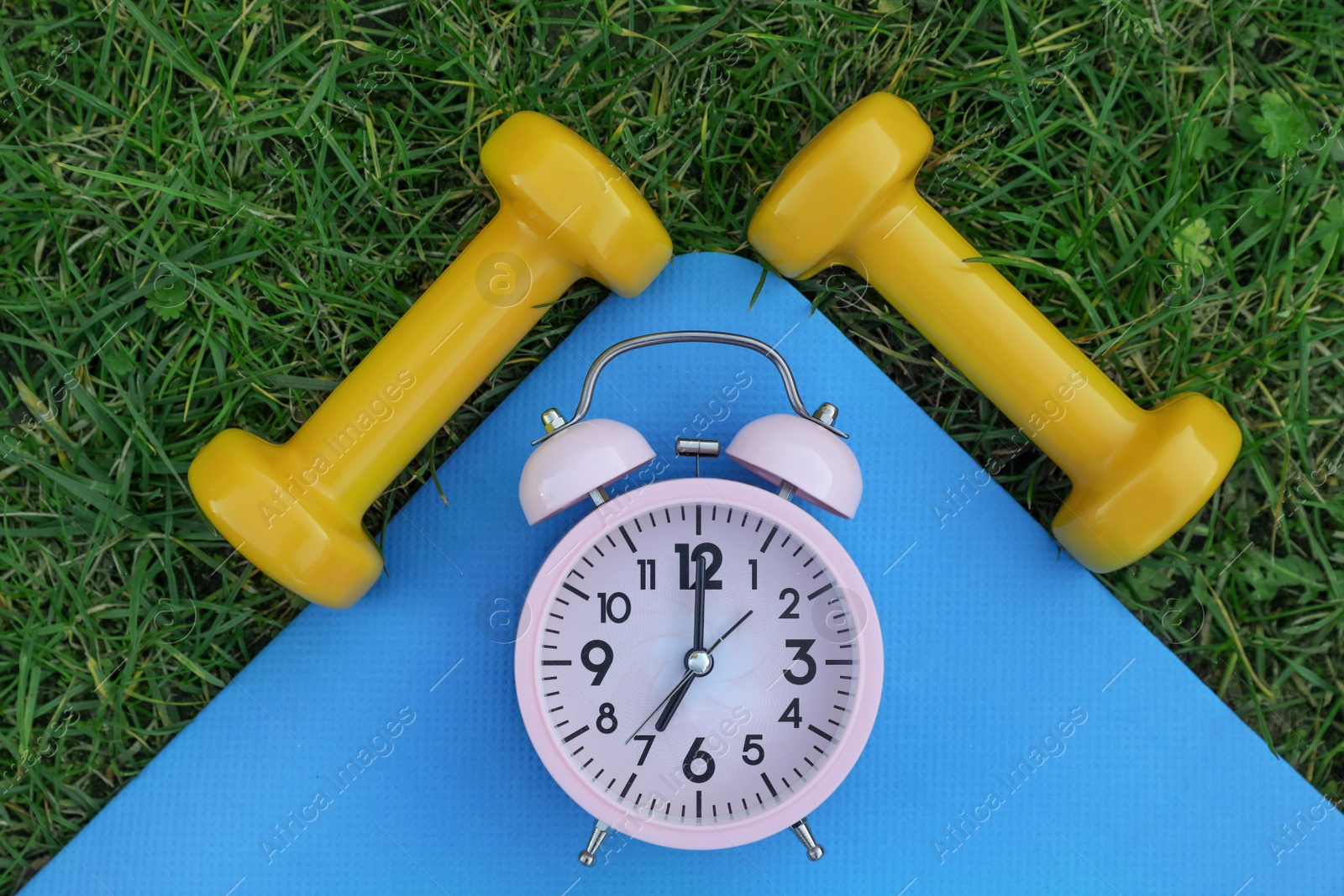 Photo of Alarm clock, dumbbells and fitness mat on green grass, flat lay. Morning exercise